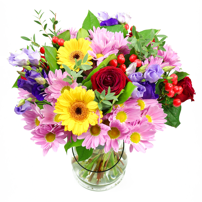 A generous, garden-style bouquet overflows from a clear glass vase, standing alone against a bright white background so every colour and detail is easy to picture. The composition centres on plush, ruby-red roses whose velvety petals fold inward in elegant spirals, giving the arrangement both depth and a sense of timeless romance. Nestled near them are vibrant yellow gerbera daisies, each bloom with a ring of smooth, radiating petals around a dark brown-orange centre, like miniature sunbursts beaming from within the design. Encircling these focal flowers is a soft cushion of pink and pale lavender daisies or chrysanthemums, their many slender petals and tiny yellow centres creating a gentle, almost feathery volume that softens the bold tones of the roses and gerberas. Threaded throughout, you can imagine the cool elegance of lisianthus in shades of purple and lilac, their bell-shaped buds and ruffled, open flowers creating layers of interest as they curve between the other stems. Here and there, small sprays of round red hypericum berries peek out from the greenery, glossy and jewel-like, adding a contemporary twist and a tactile contrast to the petals. Rich, varied foliage wraps the bouquet in shades of green, from deep, substantial leaves to lighter, more delicate stems that arch outward, echoing the natural movement of a walk through Memorial Park or along the leafy streets near Chingford Green. The vase itself is simple and clear, revealing an orderly grid of stems immersed in clean water, a quiet reminder of professional floristry skills at work. Altogether, the bouquet feels joyful yet composed, perfectly suited to mark birthdays, anniversaries, or a warm thinking of you delivery anywhere across Chingford.